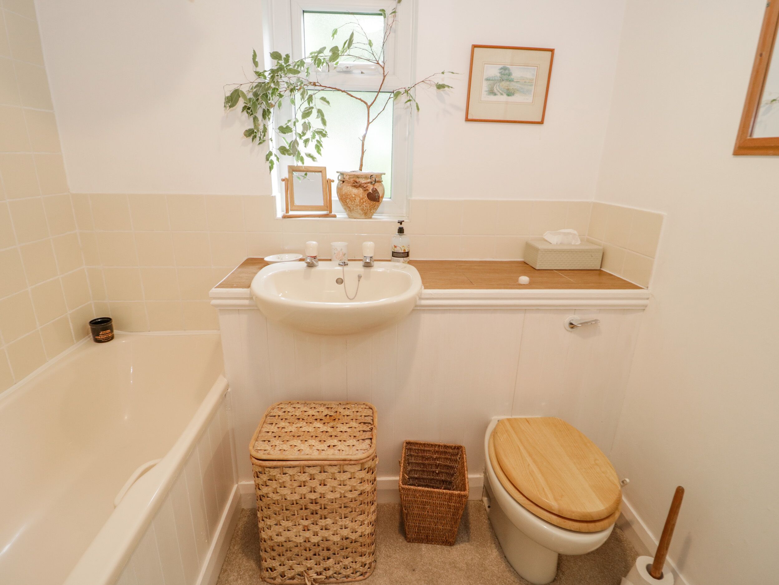 A bathroom with a bathtub, a sink, a toilet, and a small window with a plant.