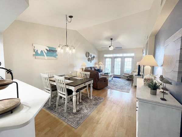 A spacious living area with a dining table, chairs, a sofa, and a ceiling fan.