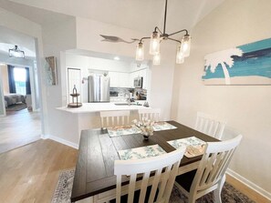 A modern kitchen with white cabinets, a central island, and a dining area with a wooden table and white chairs.