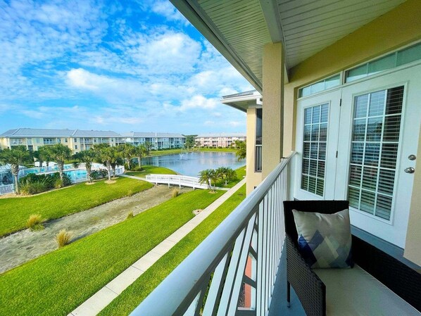A balcony with a view of a swimming pool and a body of water, surrounded by greenery and buildings.