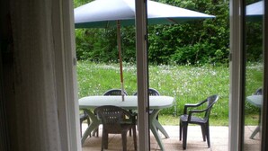 Un patio con una mesa y sillas, un paraguas verde y vistas a un jardín con flores blancas.