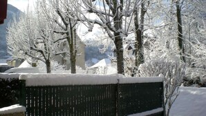 Paisaje nevado con árboles desnudos y un edificio al fondo.
