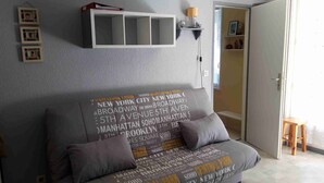 Una sala de estar con un sofá gris con texto impreso, un estante blanco montado en la pared y una puerta que conduce a otra habitación.