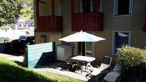 Un patio con una mesa, sillas, una sombrilla blanca y una pequeña zona ajardinada.