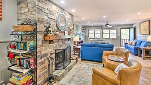 A cozy living room with a stone fireplace, a blue sofa, leather chairs, and a bookshelf filled with books. - Main St Red River Ski Condo w/ Mountain View! (Red River)