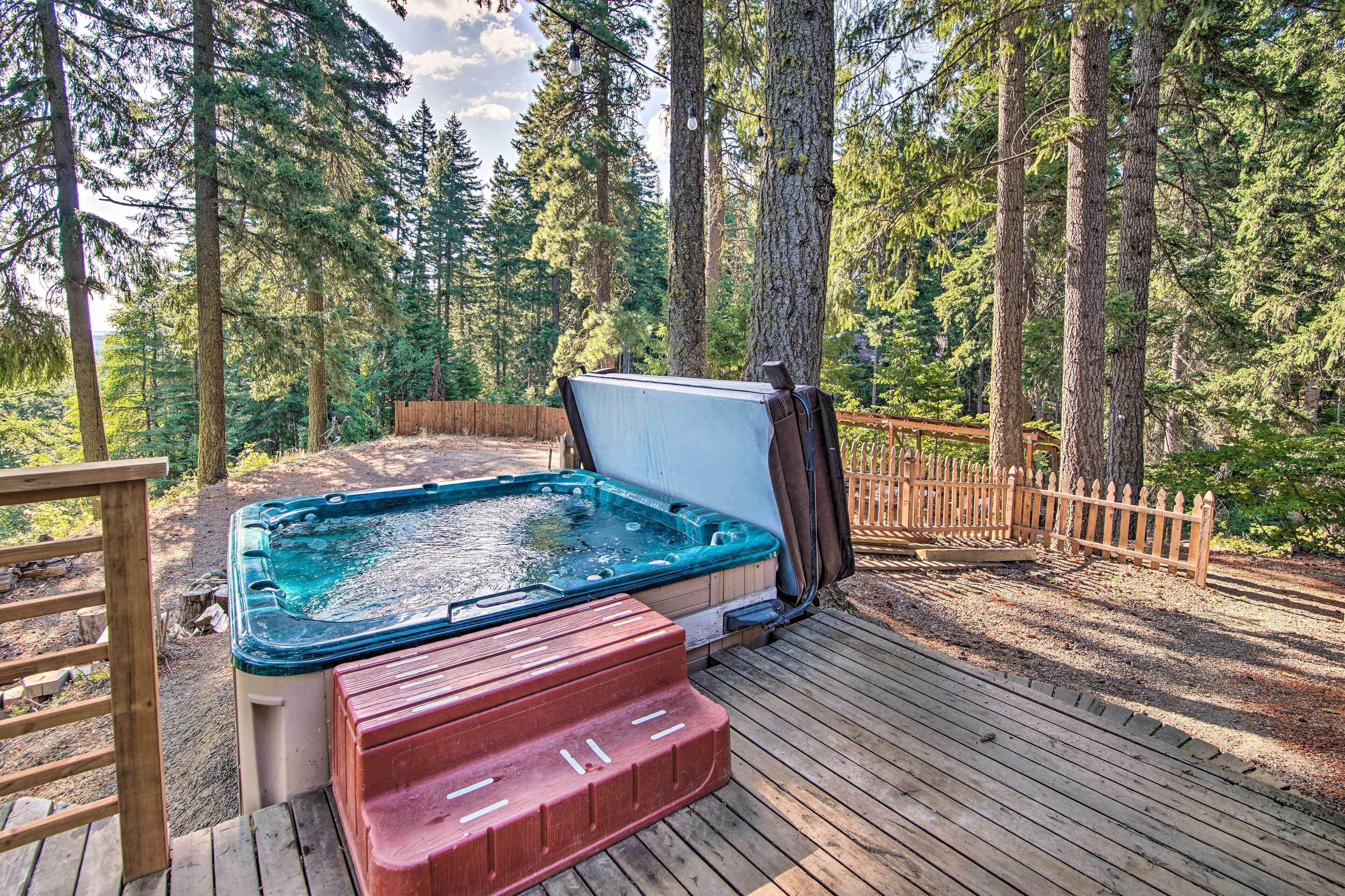 Un jacuzzi en una terraza de madera rodeado por una valla de madera y árboles altos.