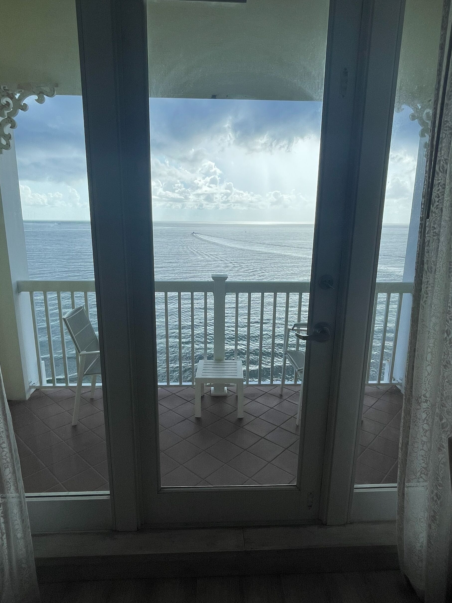 A balcony with a view of the ocean, a white chair, and a small table.