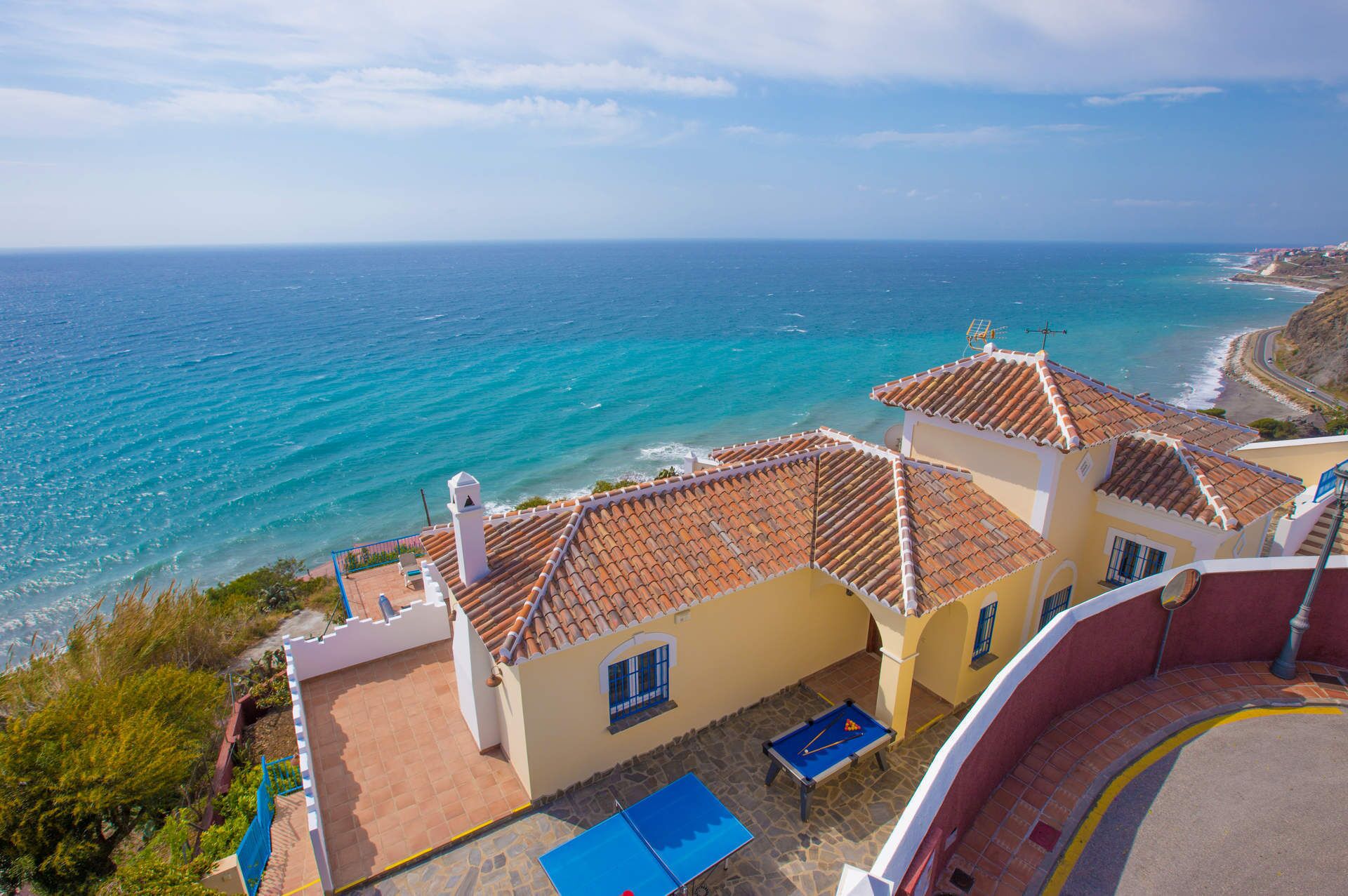 A coastal building with a pool, terracotta roofs, and a view of the sea.