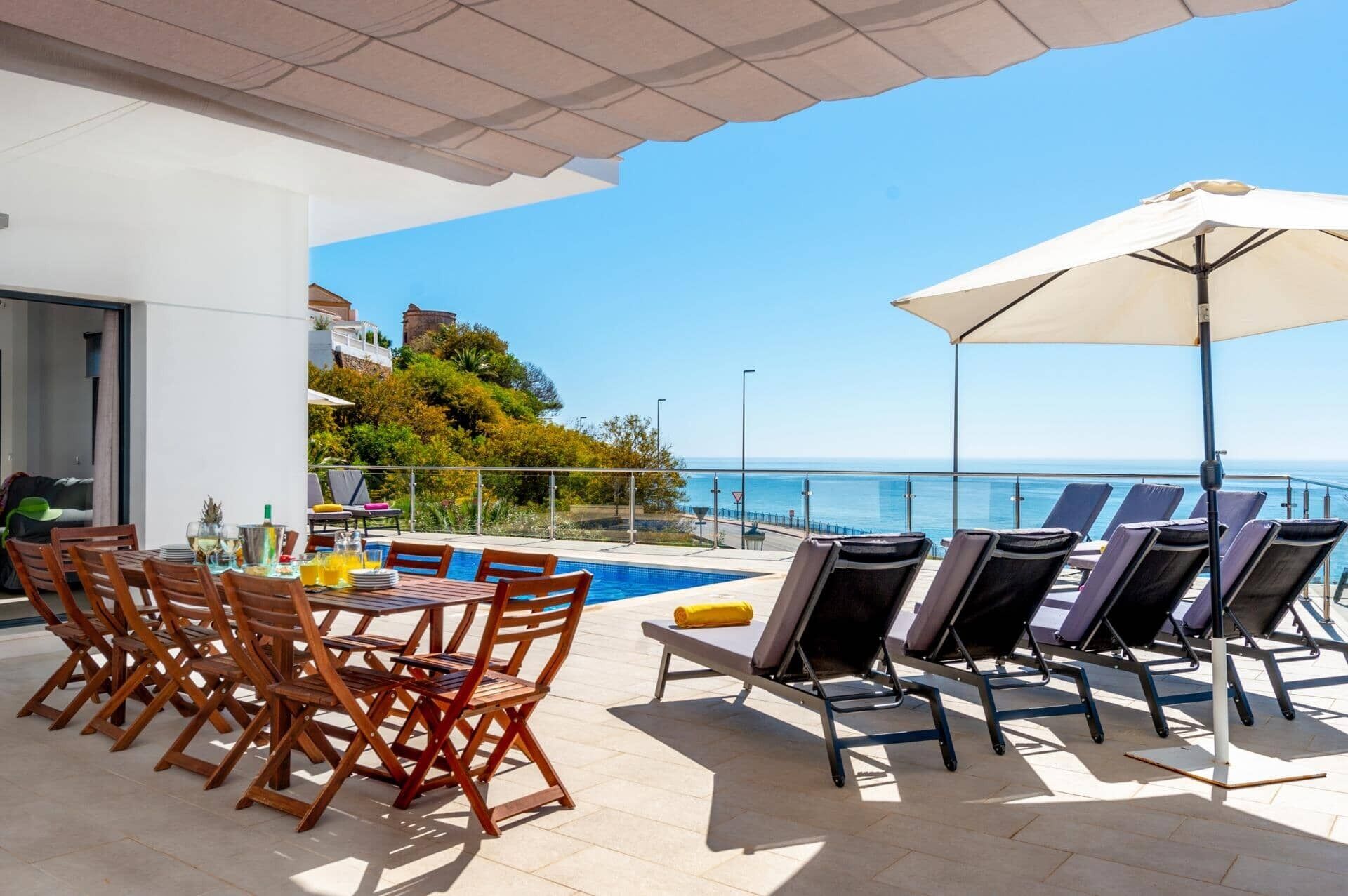 Un espace aménagé au bord de la piscine, avec une table et des chaises, une piscine, ainsi que des chaises longues dotées de parasols.