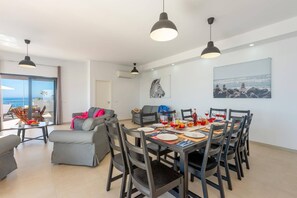 A dining area with a table set for six, surrounded by chairs, and a sofa in the background.
