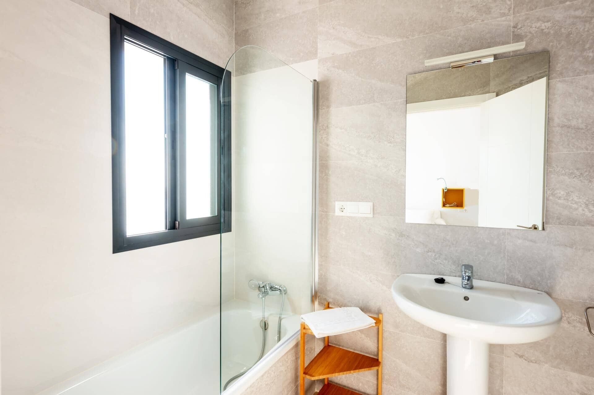 A bathroom with a glass shower enclosure, a white sink, and a mirror.
