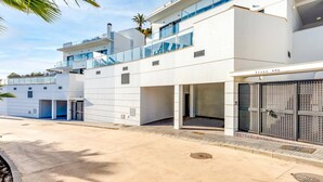 A modern multi-story building with a flat roof, large windows, and a covered outdoor area.