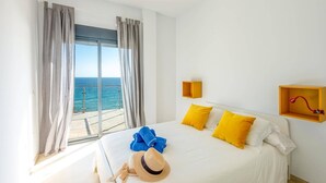 A hotel room with a bed, a view of the sea, and a small yellow shelf.