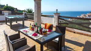 Un espacio al aire libre cubierto con mesa de billar, mesa de comedor para dos personas y sillas de mimbre.