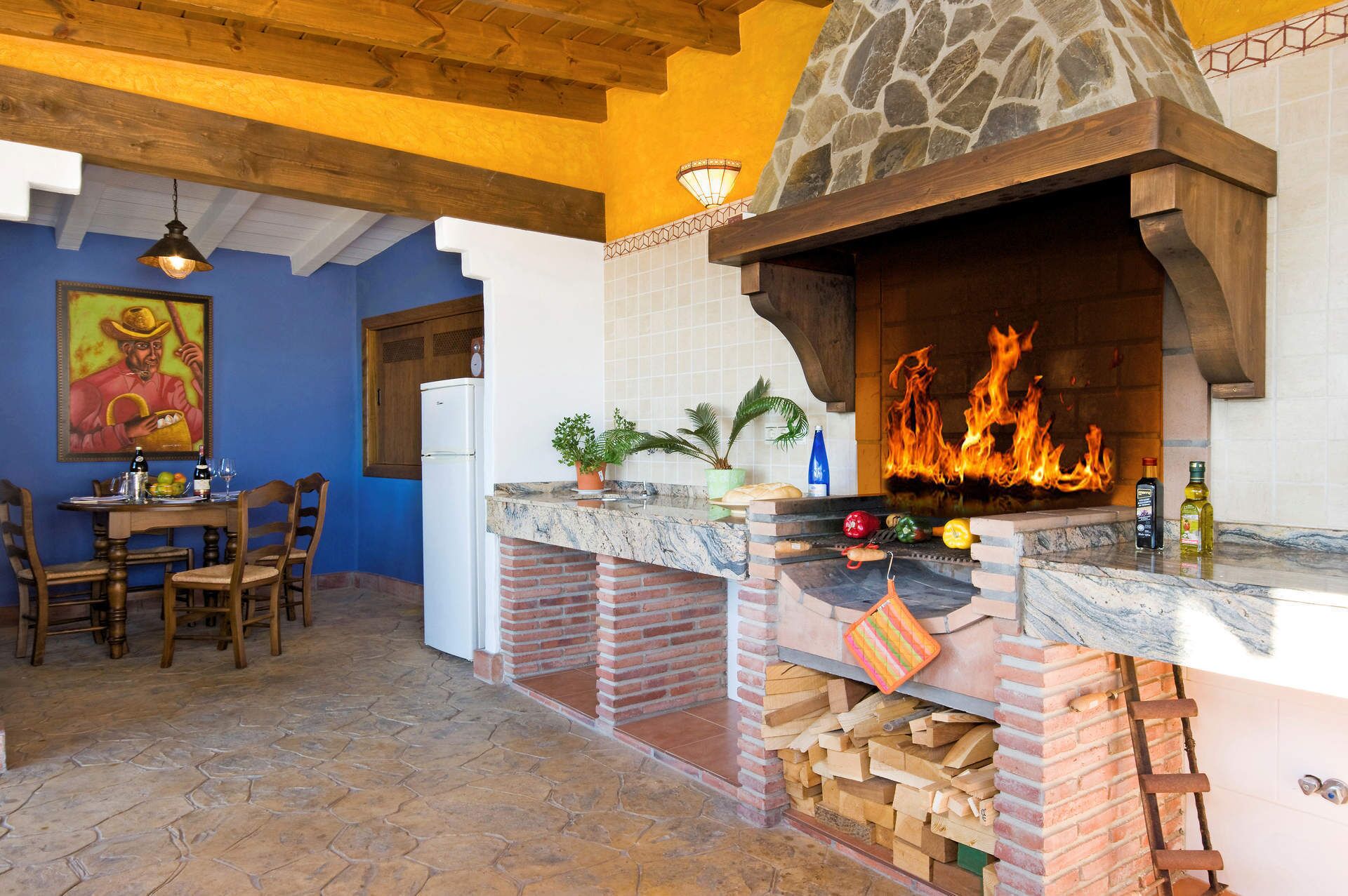 A kitchen with a stone oven, wooden ceiling beams, and a dining area with chairs and a table.