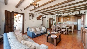 Un interior rústico con vigas de madera a la vista, una zona de comedor y una sala de estar con sofá y mesa de centro.