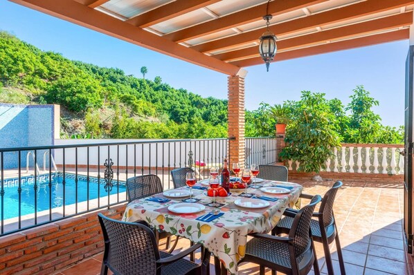 Une terrasse avec une piscine, une table à manger pour quatre personnes et une vue sur une colline verdoyante.
