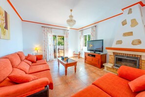 Un salon avec des canapés orange, un téléviseur, une cheminée et un balcon avec des rideaux.
