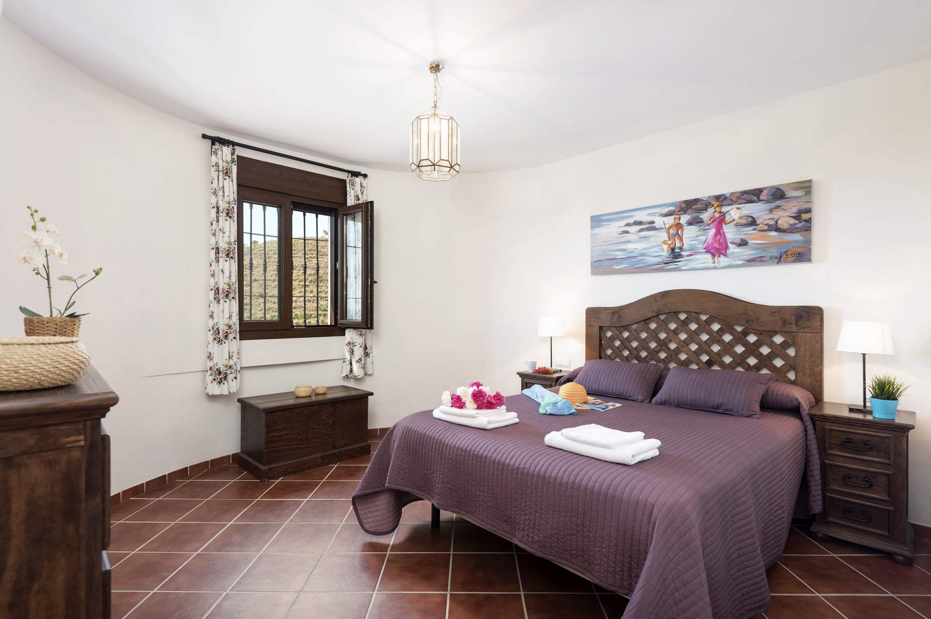 Une chambre à coucher avec un grand lit, une fenêtre avec des rideaux, un tableau au mur et une table de chevet avec une lampe.