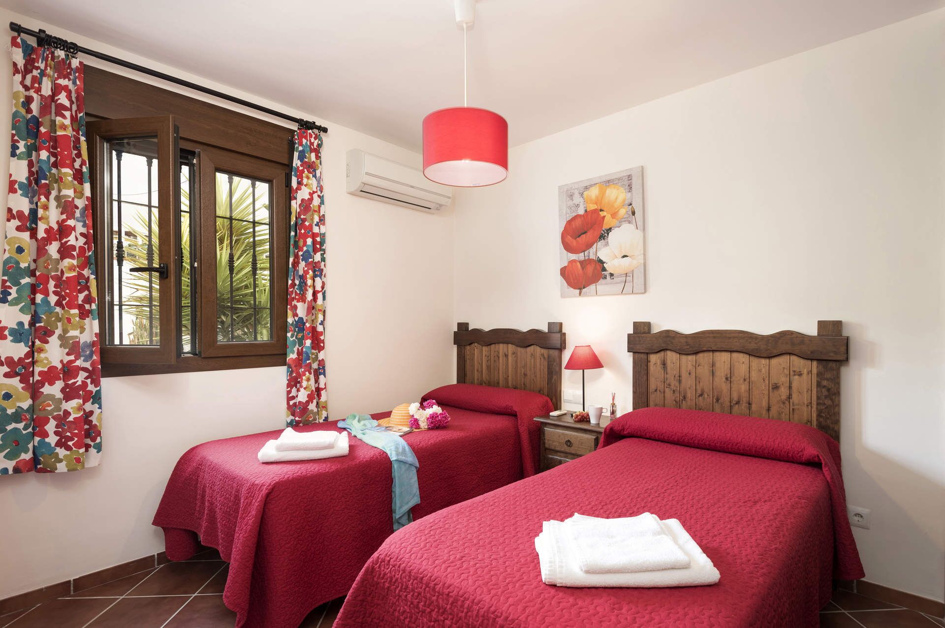 A room with two beds, a window with curtains, a lamp, and a painting on the wall.