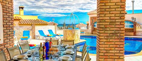 Uma área de refeições à beira da piscina, com uma mesa posta para seis pessoas, com vista para a piscina e o mar.