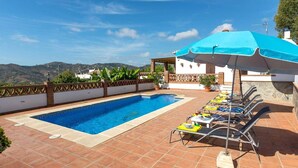 Une piscine dotée de chaises longues et d’un espace abrité, entourée d’une terrasse carrelée et offrant une vue sur les collines.