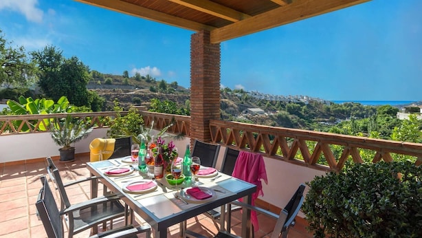 Une terrasse avec une table dressée pour le repas, offrant une vue sur un paysage côtier.
