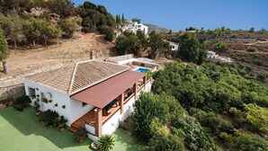 Une villa blanche, dotée d’un toit en tuiles et d’une piscine, entourée de verdure et de collines.