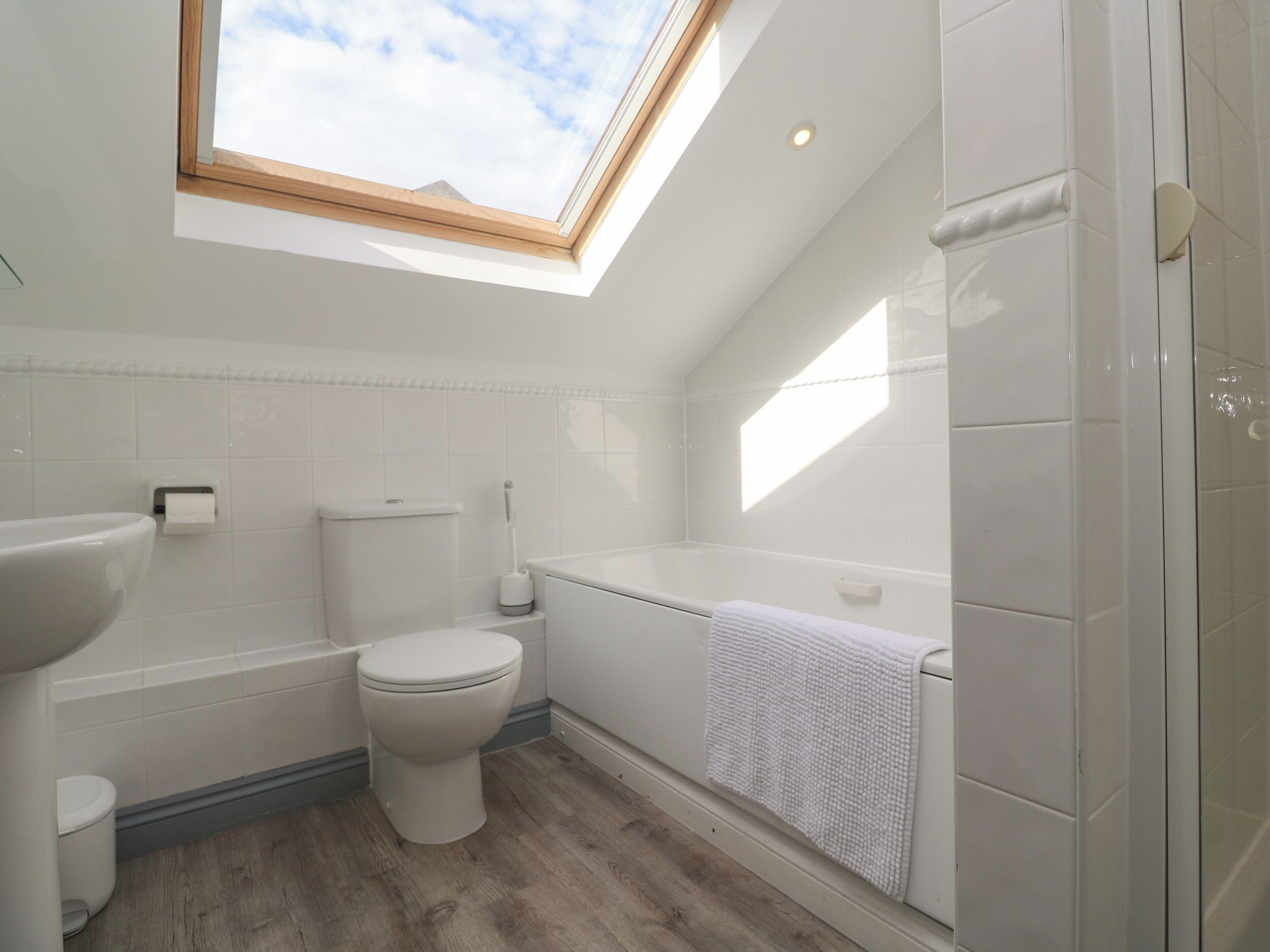 A modern bathroom with a skylight, a toilet, a bathtub, and a sink.