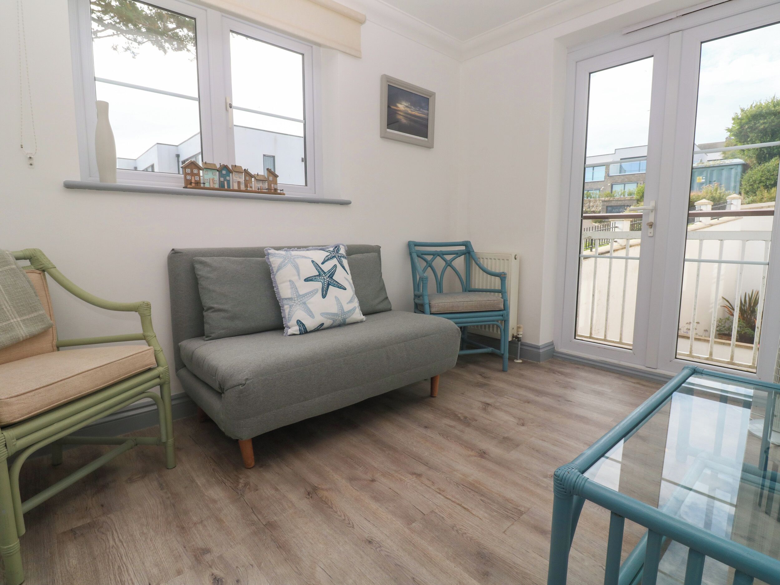 Una habitación con un sofá gris, una silla azul, una mesa de vidrio y una ventana con vistas a edificios.
