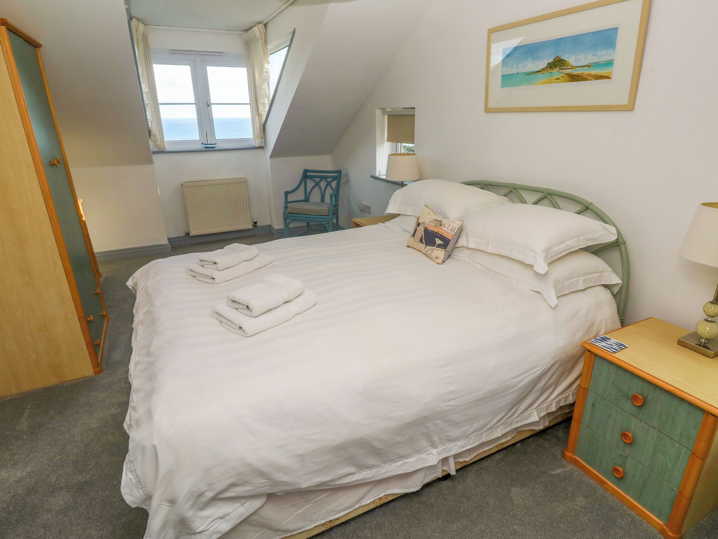 Un lit bien fait, avec du linge de lit et des serviettes blanches, une tête de lit verte, une table de chevet avec une lampe et un tableau encadré au mur.
