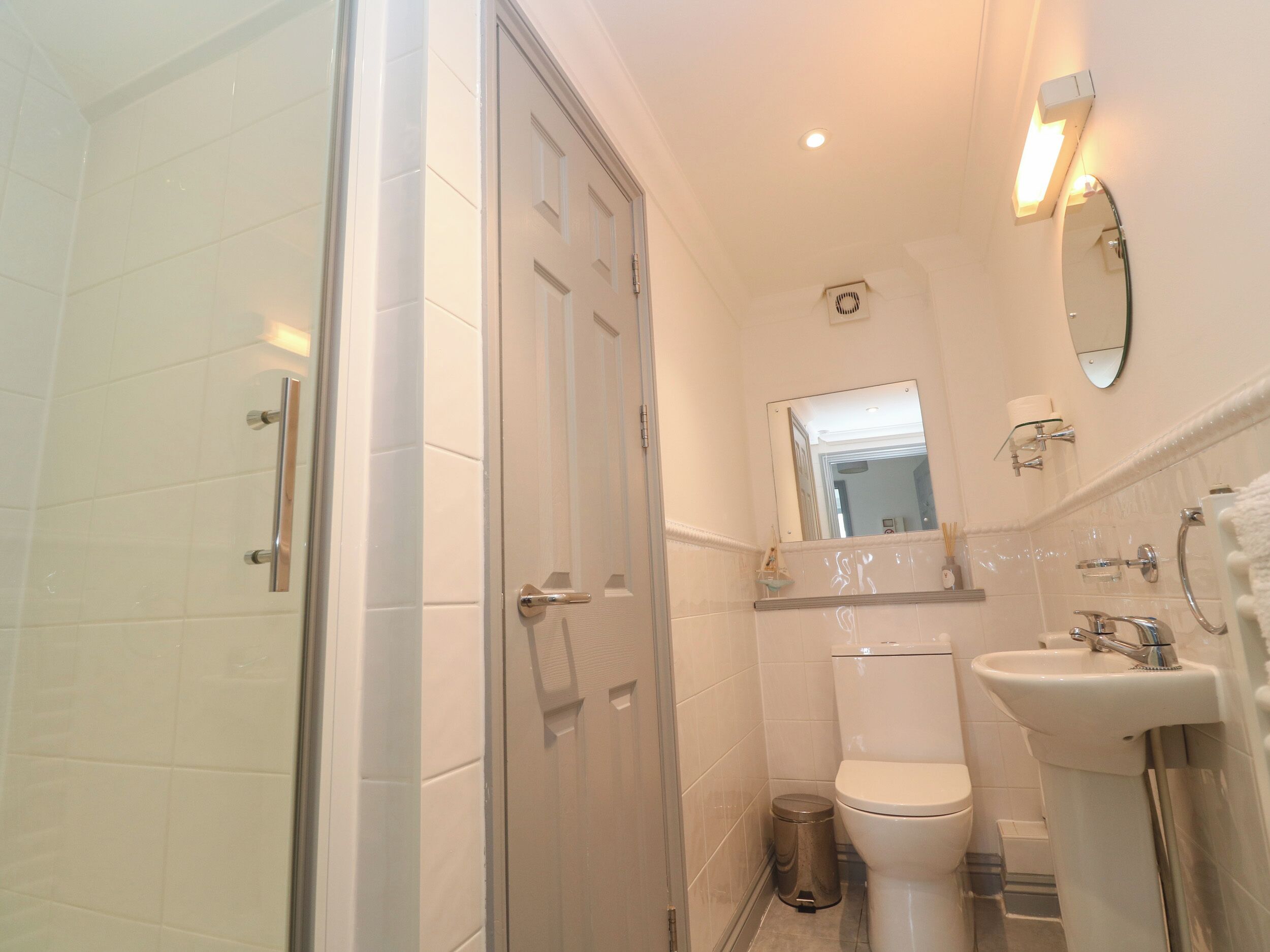 A bathroom with a glass shower enclosure, a toilet, a sink, and a mirror.
