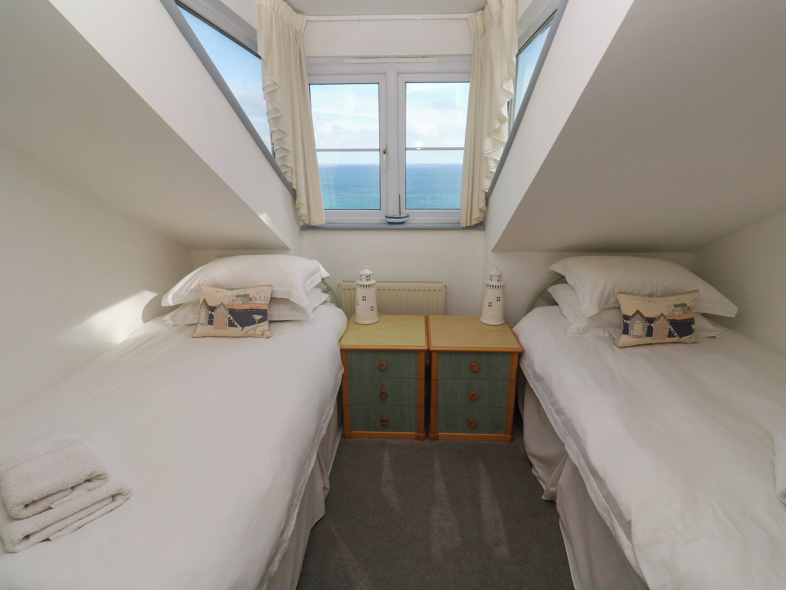 A small, well-lit bedroom with two beds, a nightstand, and a window with a view of the sea.