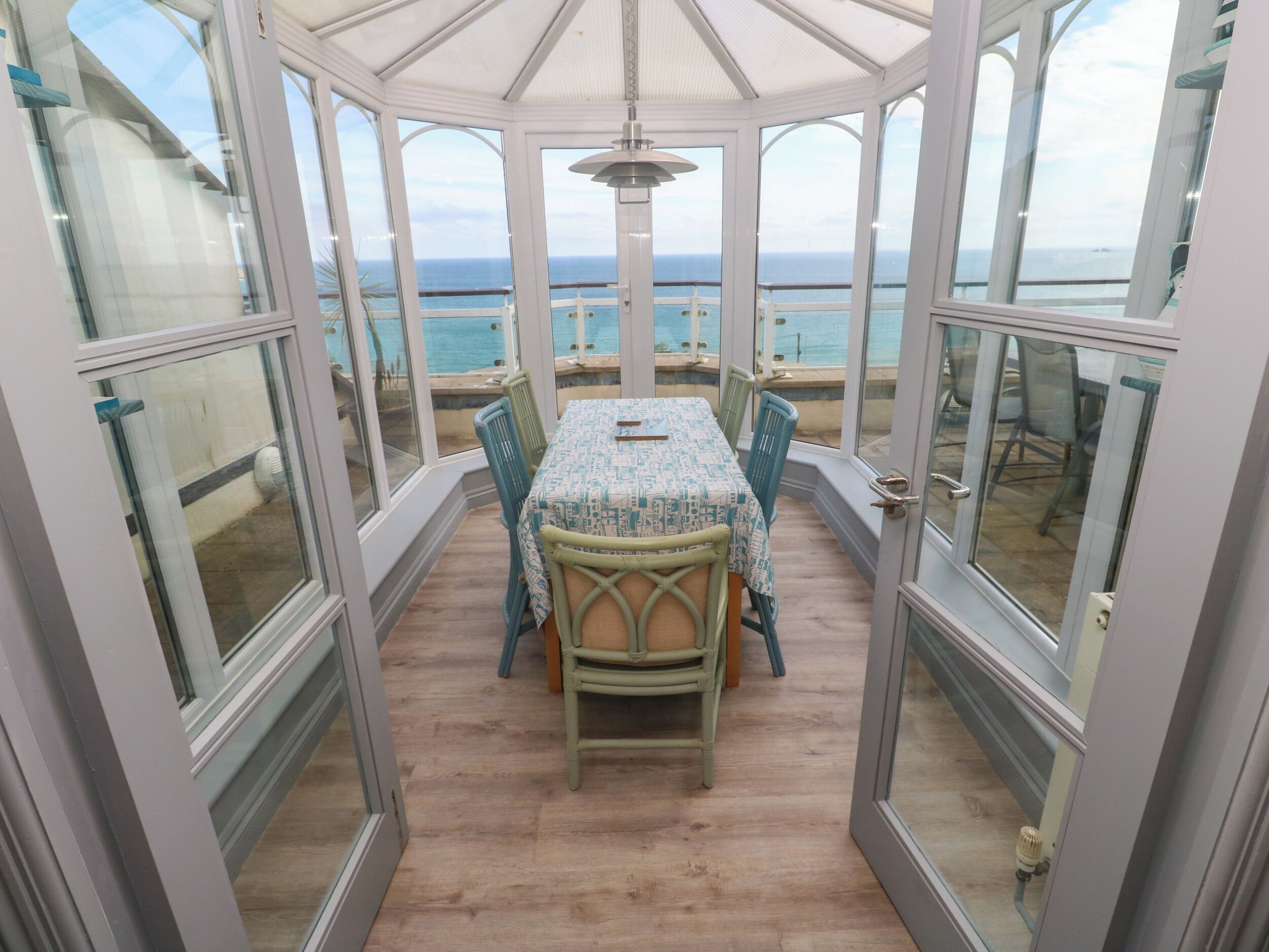A conservatory with a table and chairs, large windows, and a view of the sea.
