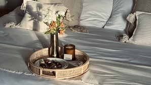 A neatly made bed with white linens, a vase with flowers, and a tray with chocolates and a bottle of wine. - Hotel Sureño Yucatán (Mérida)