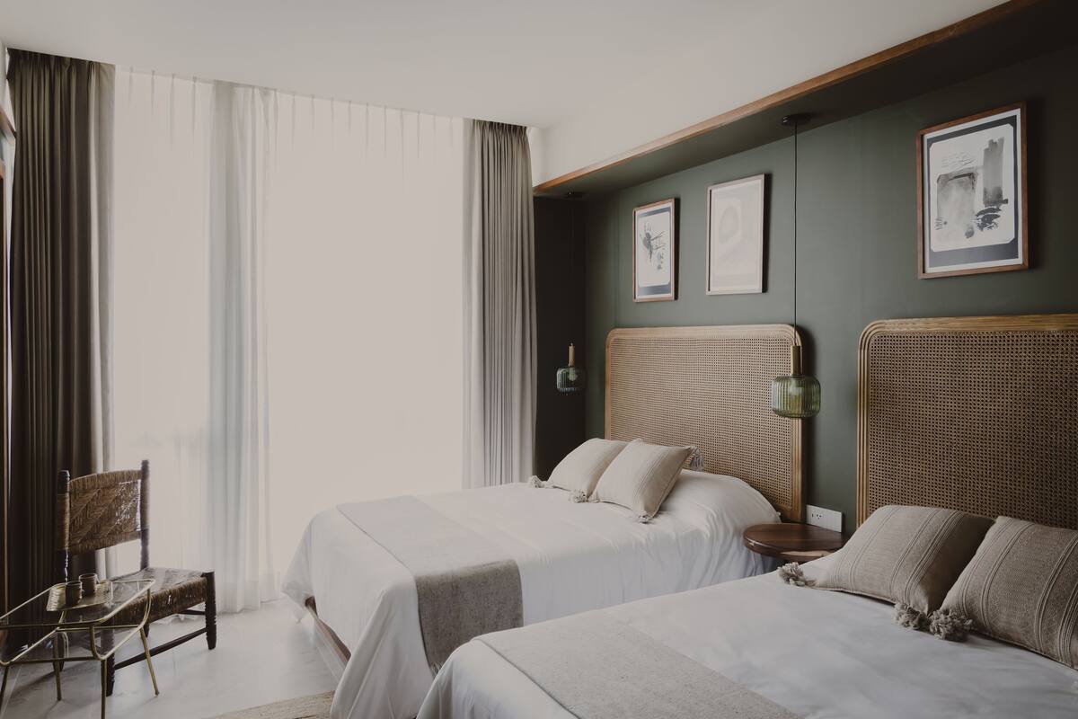 A hotel room with two beds, a chair, and a wall-mounted lamp.