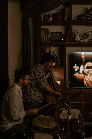 A room with a drum set, a television displaying candles, and a shelf with various items. - Hotel Sureño Yucatán (Mérida)