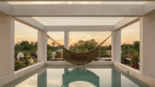 A hammock over a pool with a view of trees and a sunset. - Hotel Sureño Yucatán (Mérida)