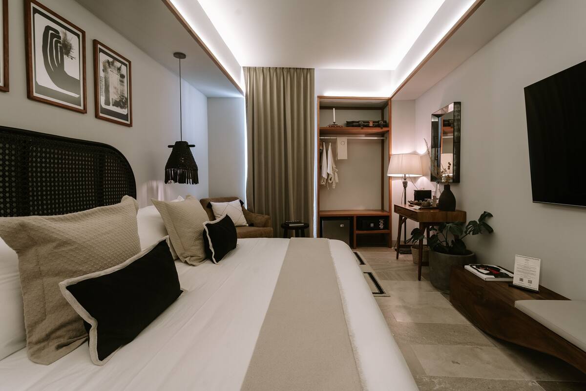 A hotel room with a large bed, bedside table, desk, and wardrobe.