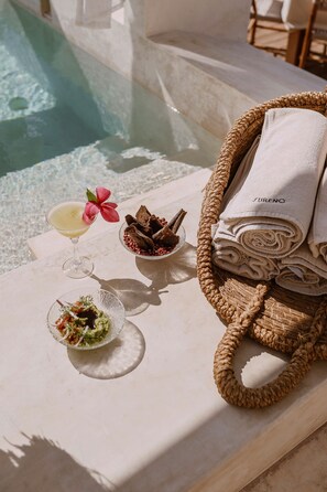 A poolside setting with a glass of cocktail, a bowl of chips, and a plate of food. - Hotel Sureño Yucatán (Mérida)