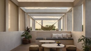 A modern outdoor seating area with a hammock, a bench with cushions, and a round table with a bowl of fruit. - Hotel Sureño Yucatán (Mérida)