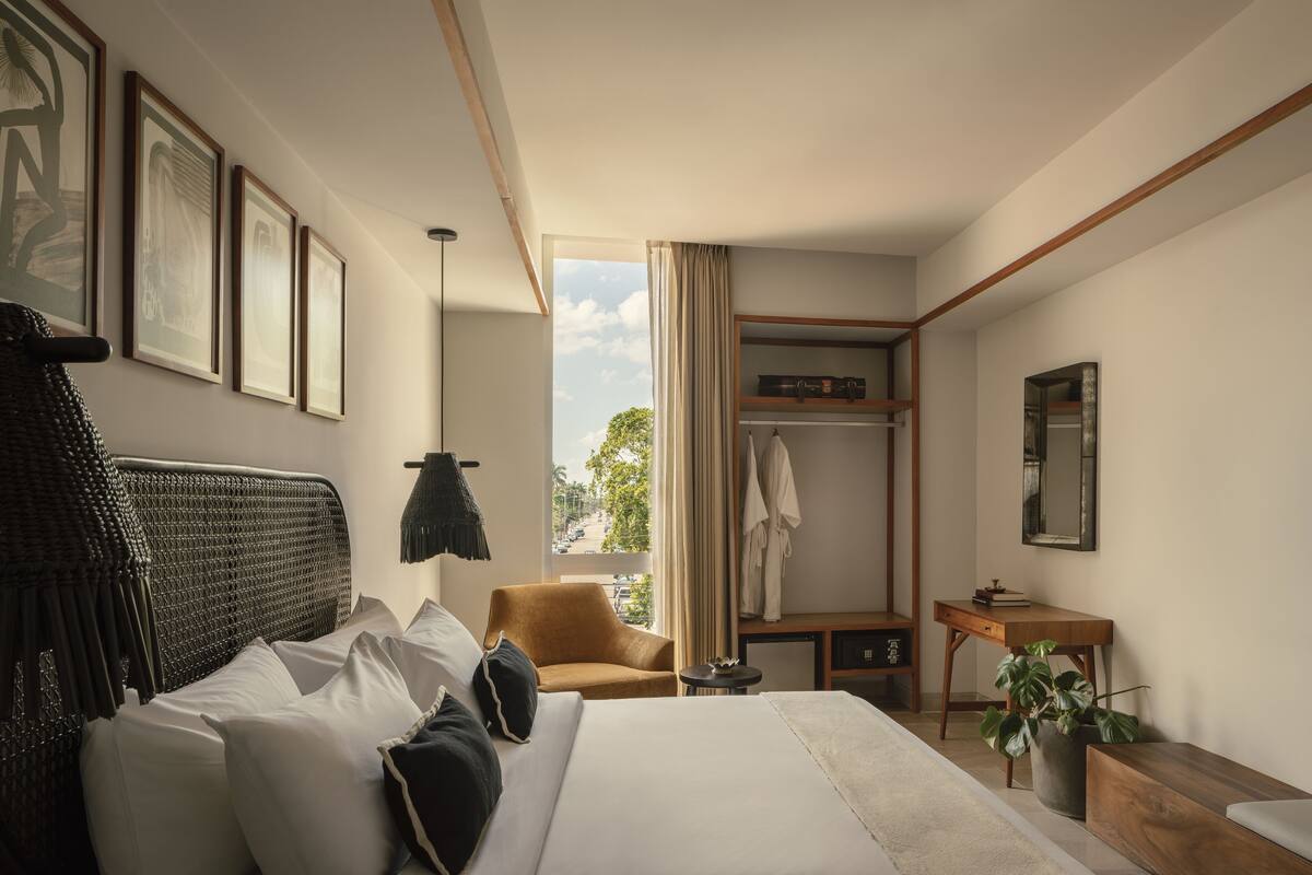 A hotel room with a large bed, a sitting area with a chair, a desk, a wardrobe, and a window with a view of the outdoors.