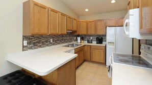 A compact kitchen with wooden cabinets, a white countertop, a built-in microwave, and a stove. - Updated Twin Home near Sanford Medical Center (West Fargo)