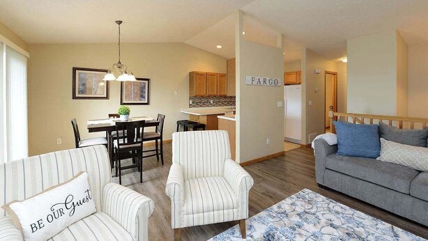 A living room with a sofa, armchair, and a dining area with a table and chairs. - Updated Twin Home near Sanford Medical Center (West Fargo)