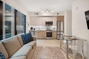 Enjoy a compact living space with a kitchenette, glass dining table, and a sofa with patterned cushions, offering a city view.