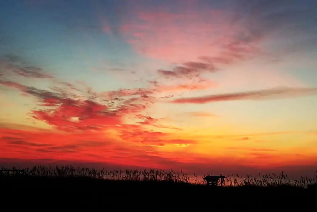 Een zonsondergang met een silhouet van een gebouw en gras op de voorgrond.