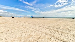 Une vaste plage de sable fin, un ciel dégagé et quelques parasols disséminés au loin.