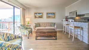 Un salon avec un canapé, une table basse et des fauteuils, une cuisine avec un bar et un balcon avec vue.