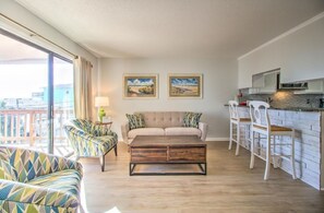 Ein Wohnzimmer mit Sofa, Couchtisch und Sesseln, eine Küche mit Bar und ein Balkon mit Blick.