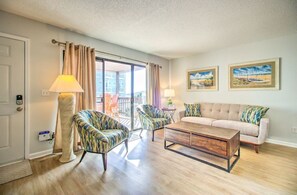 A well-lit living room with a sofa, two armchairs, a coffee table, and a balcony with curtains. - Beach Condo in great location,sleeps 6! (Carolina Beach)